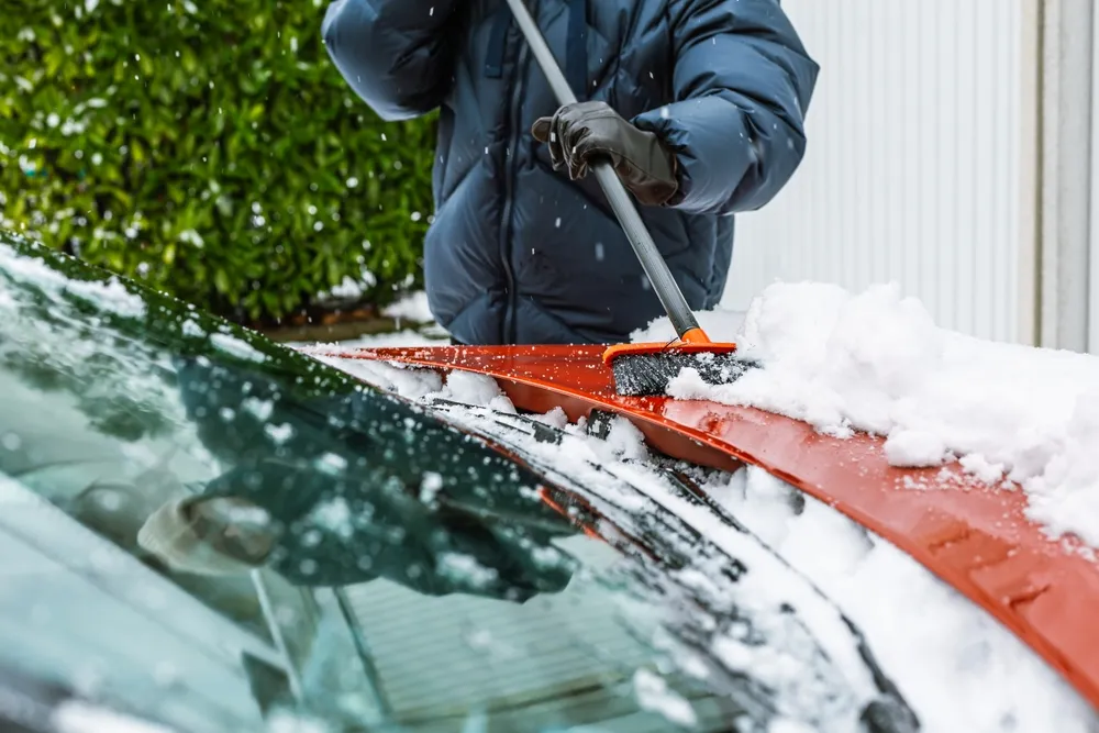Schnee vom Auto entfernen: Person räumt roten Pkw im Winter frei, Tipps für Winterpflege.